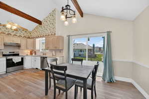 Vaulted ceiling kitchen featuring exposed wood beams, light wood-finish cabinetry, stainless steel appliances, and wood-finish flooring