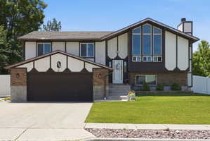 Split-level residence featuring a prominent front gable with large windows, an integrated two-car garage, and a brick facade accent