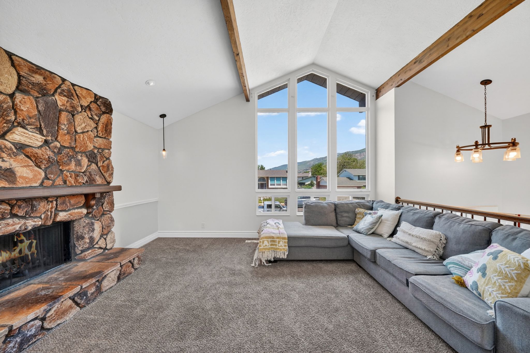 Living area featuring a stone-clad fireplace, vaulted ceilings with exposed wood beams, expansive picture windows, and a hardwood railing