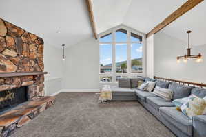 Living area featuring a stone-clad fireplace, vaulted ceilings with exposed wood beams, expansive picture windows, and a hardwood railing