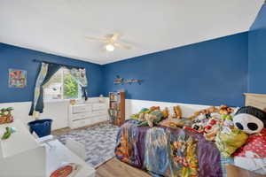 Bedroom featuring wood-finish flooring, a ceiling fan with integrated lighting, and a window with blinds