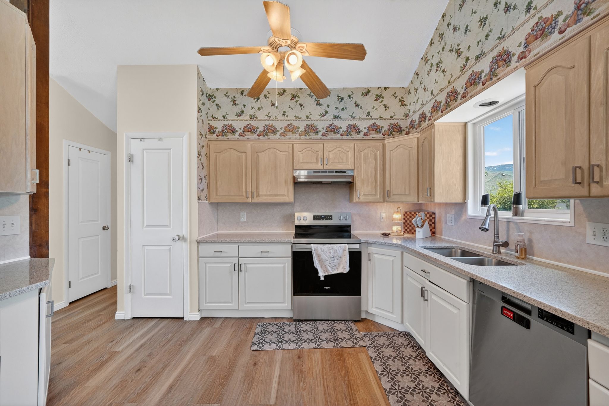Kitchen featuring wood-finish flooring, vaulted ceilings, a ceiling fan with integrated lighting, stainless steel appliances, and a double basin sink