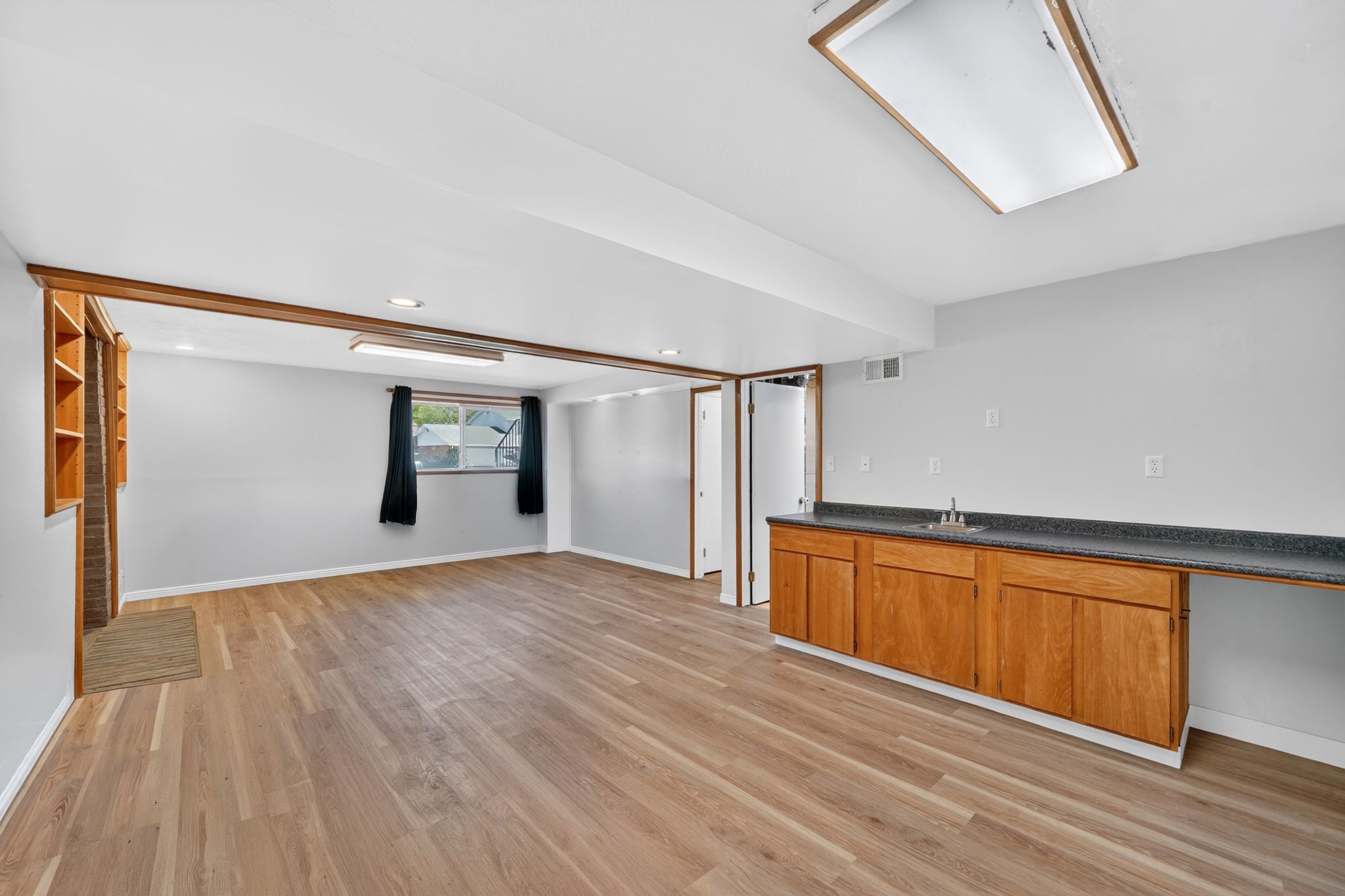 Spacious lower-level room featuring wood-finish flooring, a built-in wet bar with wood cabinetry and a dark countertop, an integrated window, and recessed lighting