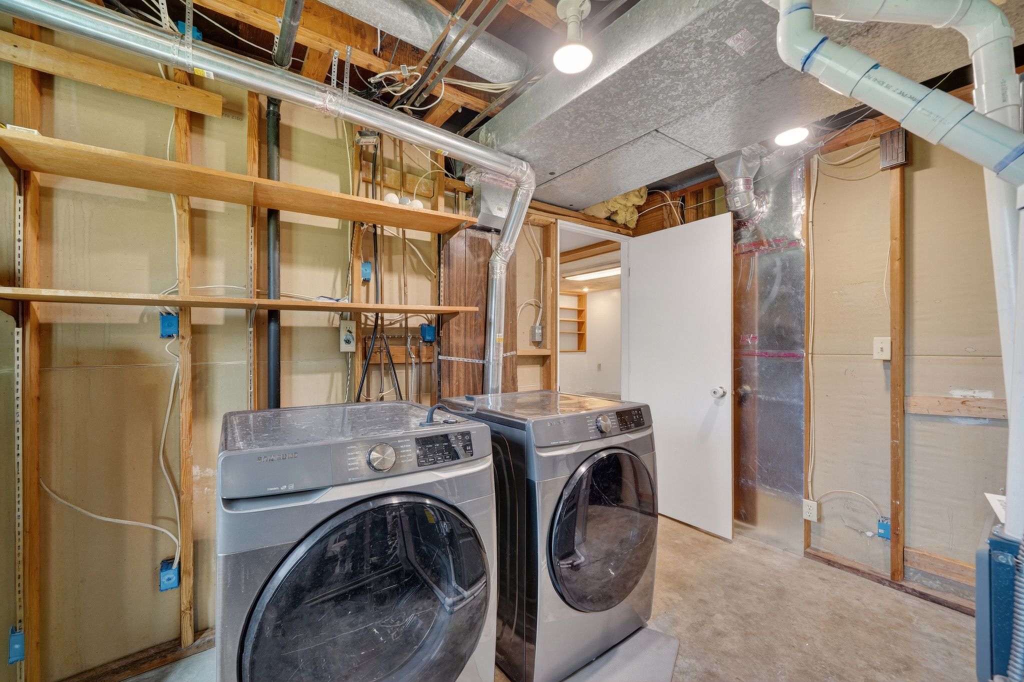 Dedicated laundry area featuring a concrete floor, overhead lighting, and built-in shelving