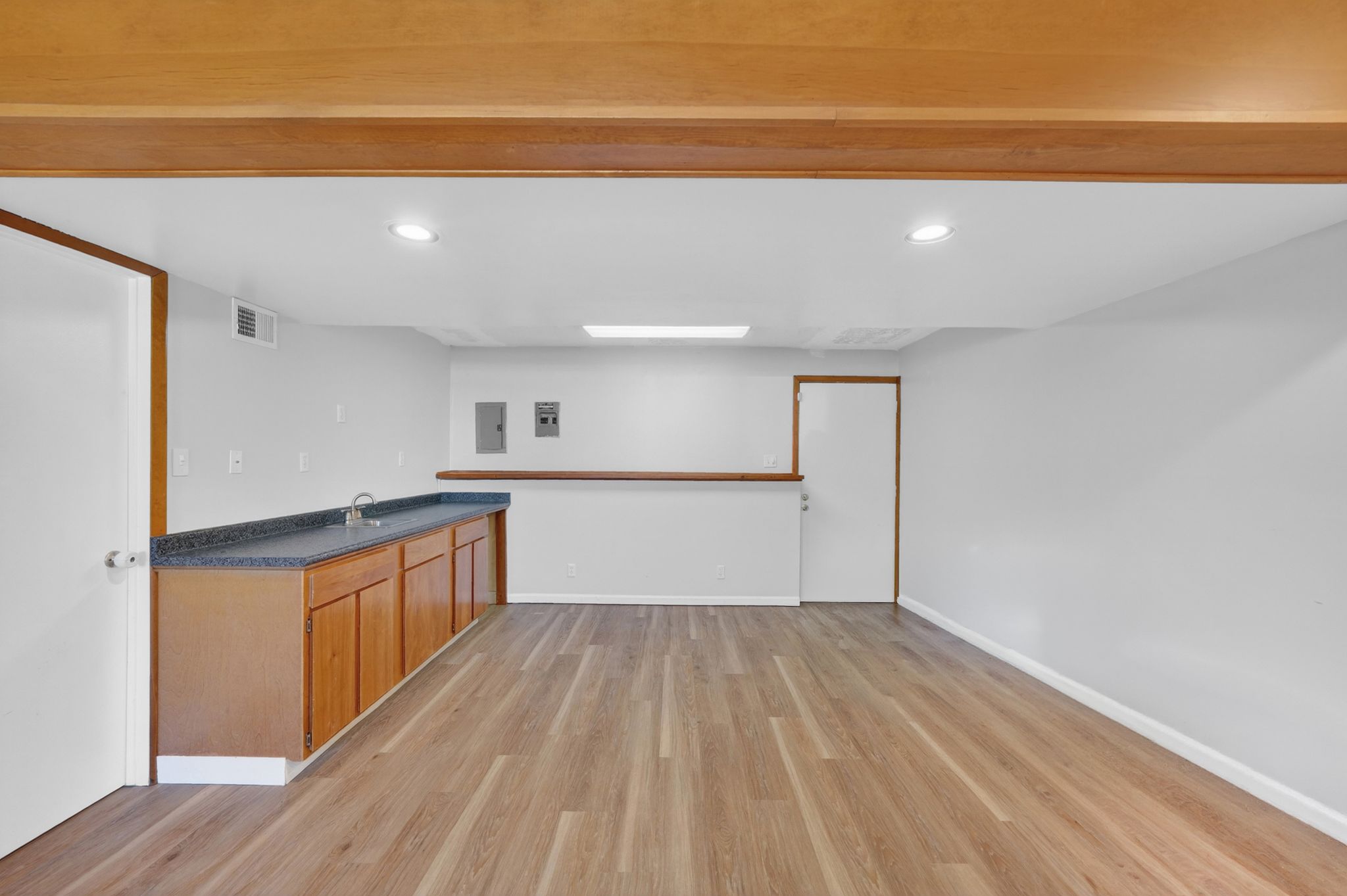 Spacious room featuring wood-finish flooring, a built-in wet bar with dark countertops and wood cabinetry, white walls, and recessed lighting