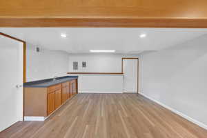 Spacious room featuring wood-finish flooring, a built-in wet bar with dark countertops and wood cabinetry, white walls, and recessed lighting