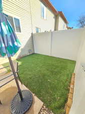 Compact outdoor space featuring a white vinyl privacy fence, artificial turf, and a concrete patio area
