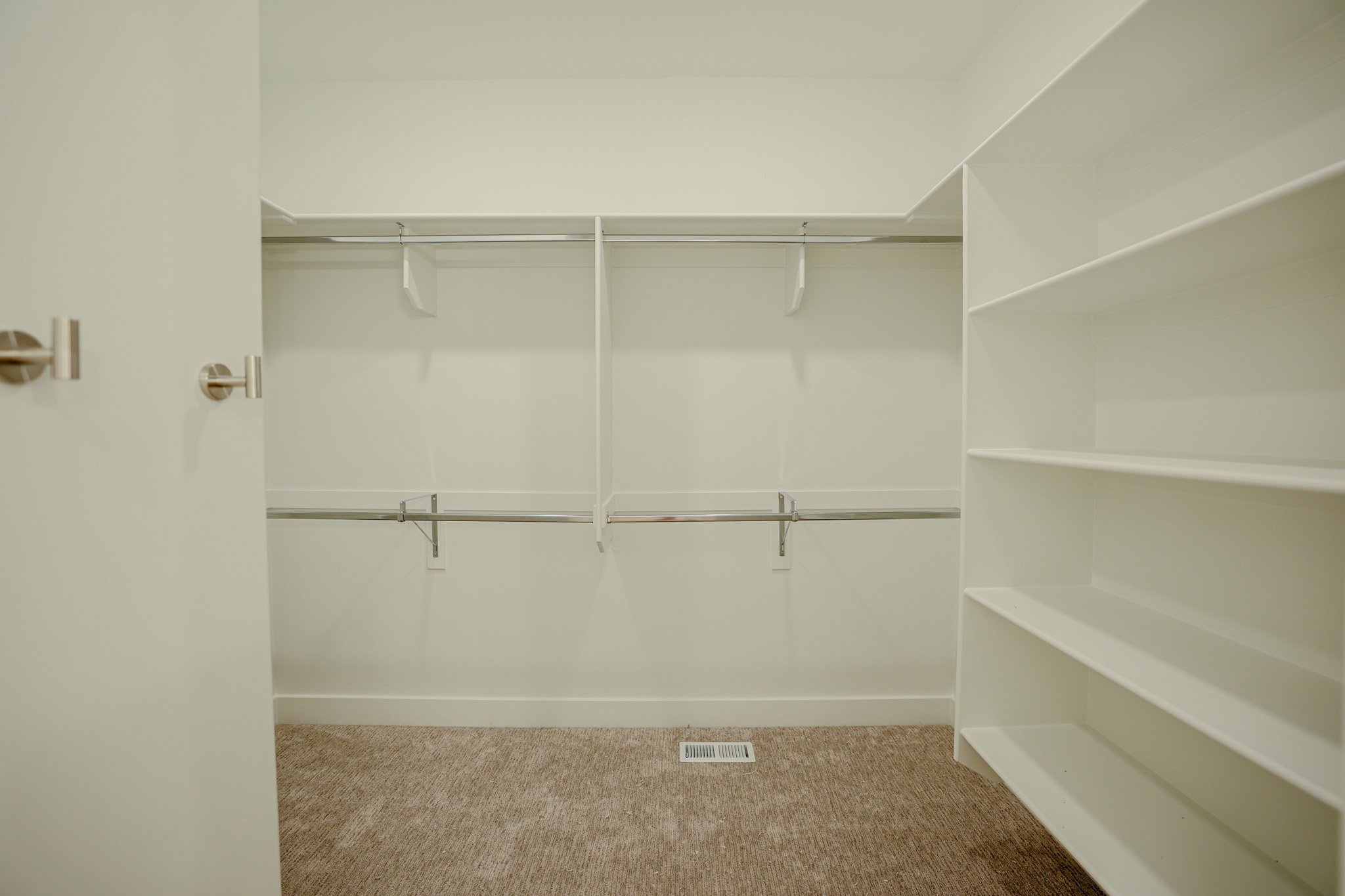 Spacious closet featuring wall-mounted shelving, multiple hanging rods, and neutral-toned carpet flooring
