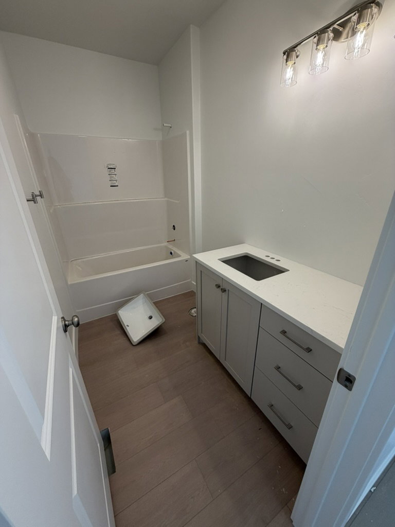 Bathroom featuring a contemporary vanity with a white countertop and undermount sink, wood-finish flooring, a three-light vanity fixture, and a white tub/shower combination