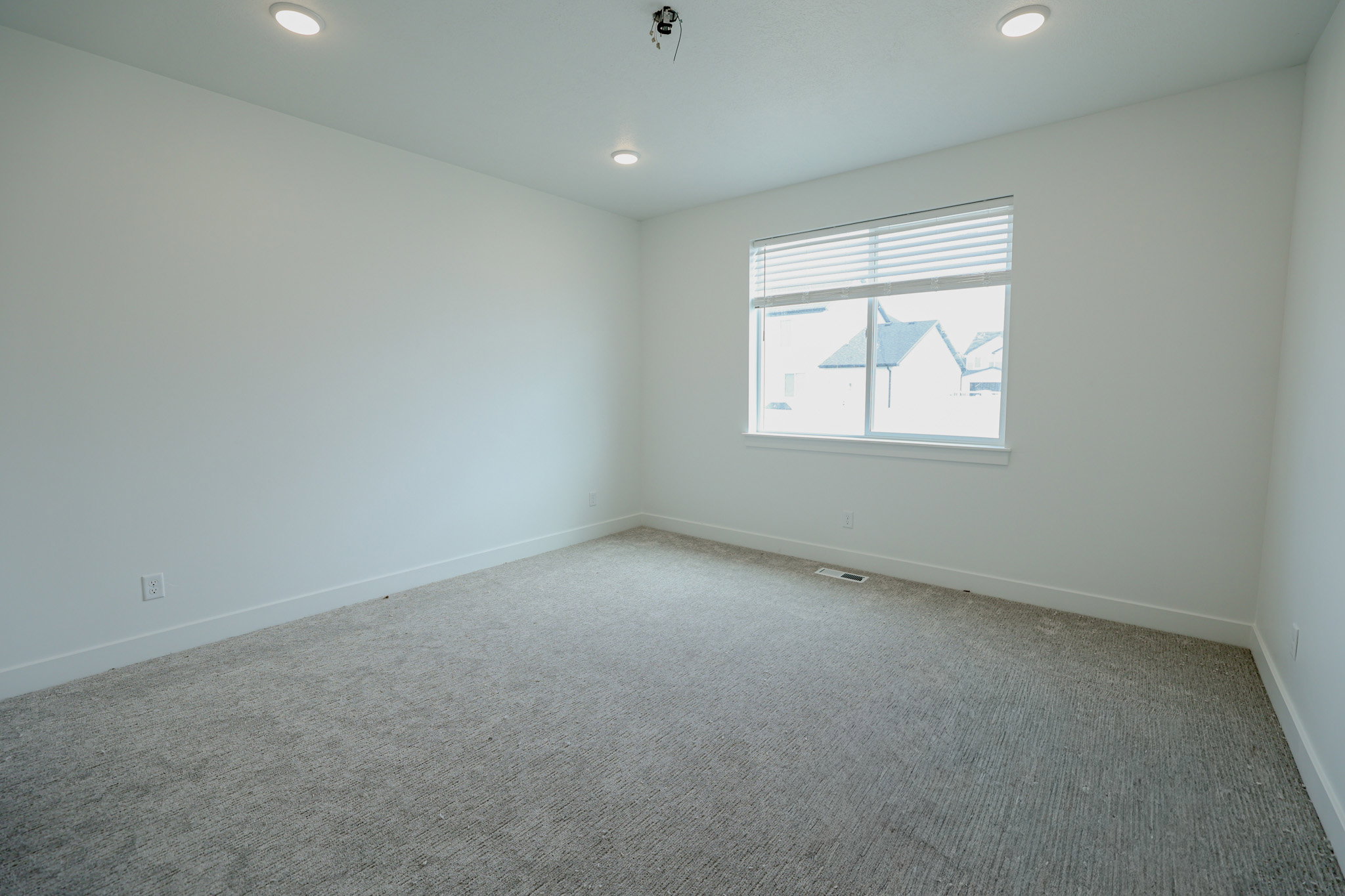 Carpeted room featuring a single window with horizontal blinds, recessed ceiling lighting, and crisp white baseboards
