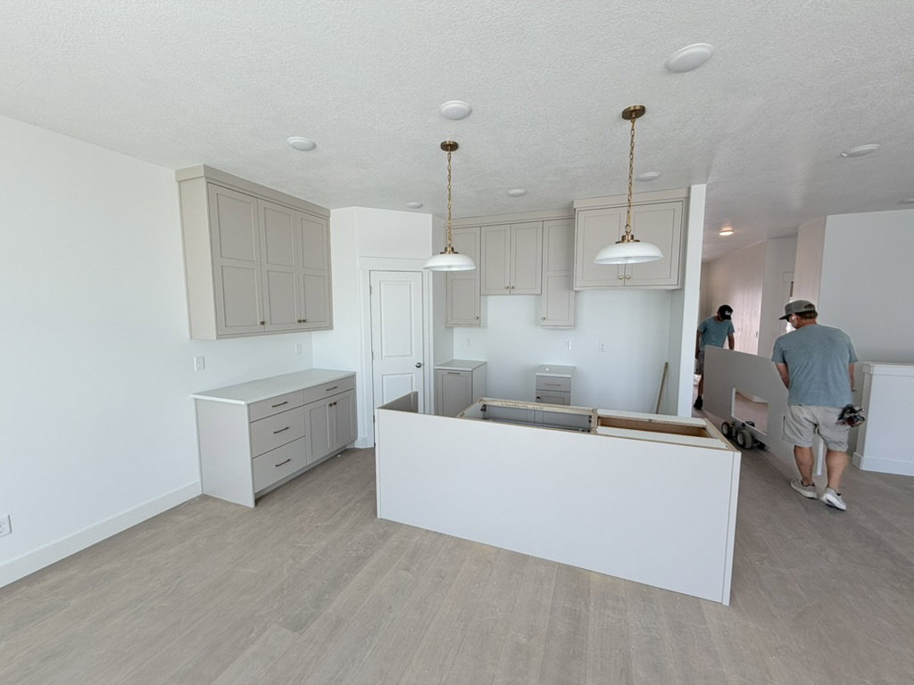 Kitchen space featuring neutral-toned cabinetry, light-colored countertops, two pendant light fixtures, recessed ceiling lighting, and wood-finish flooring