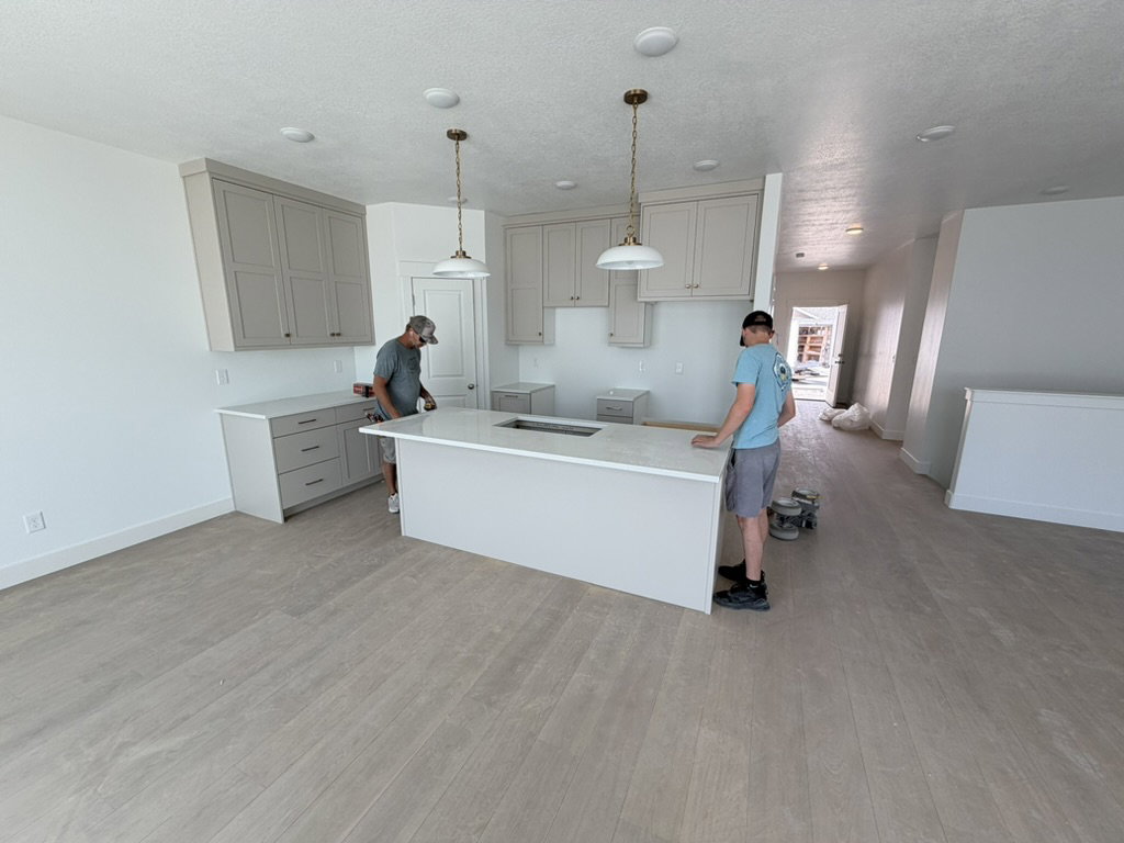 Modern kitchen featuring an expansive center island with an integrated sink, light-toned cabinetry, and wood-finish flooring