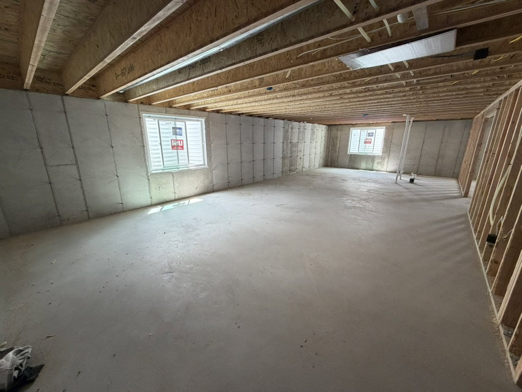 Spacious unfinished basement featuring concrete flooring, exposed wood joists, framed walls, and two visible windows