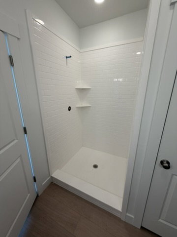 Walk-in shower with white subway tile walls, integrated shelving, and a white shower pan