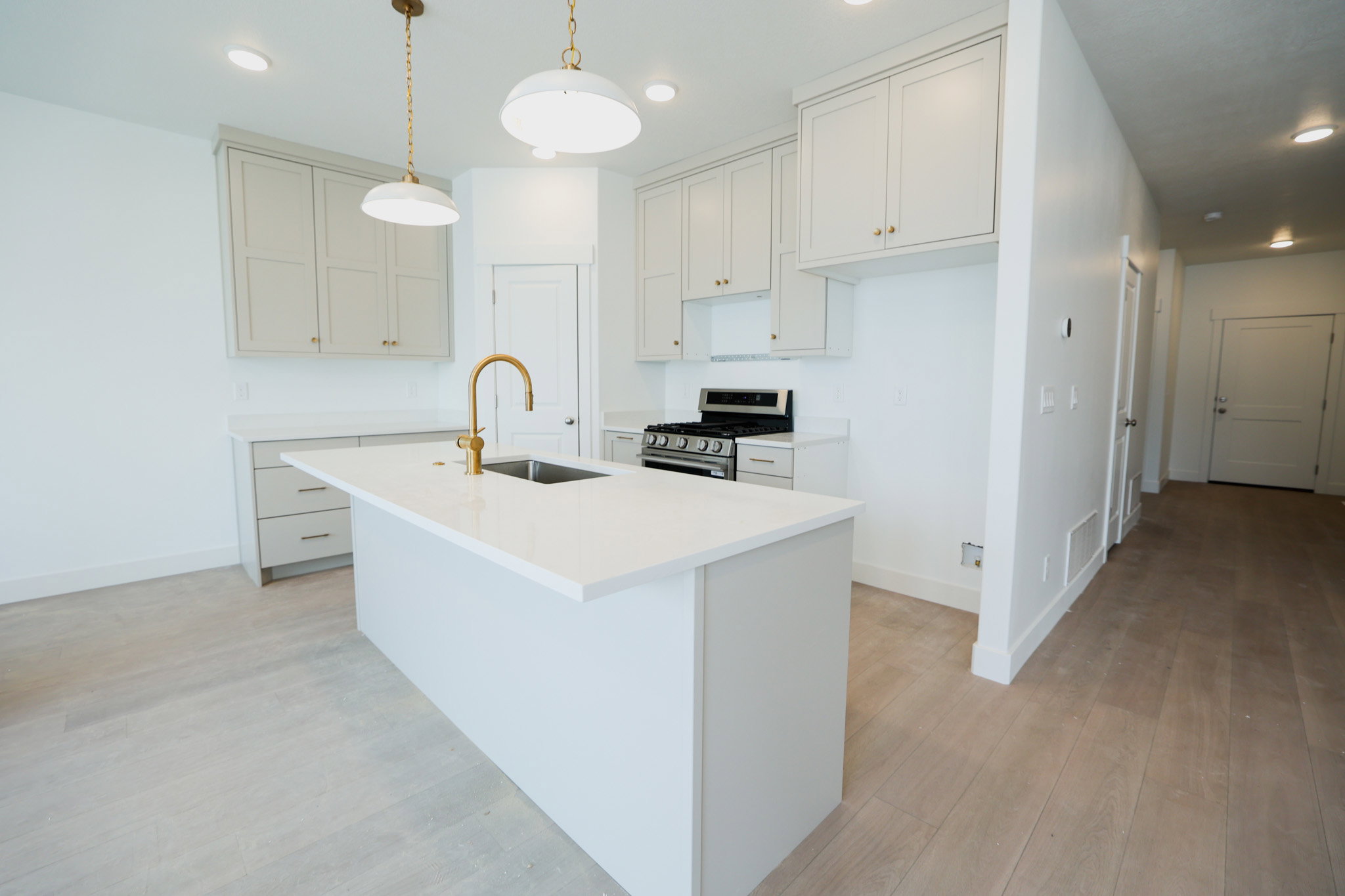 Contemporary kitchen featuring a center island with an undermount sink and brass faucet, light-colored cabinetry with brass hardware, a stainless steel range, and wood-finish flooring