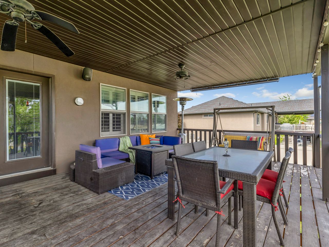 Spacious covered outdoor deck featuring wood-finish flooring, a full-light glass door, multiple windows, and a ceiling fan