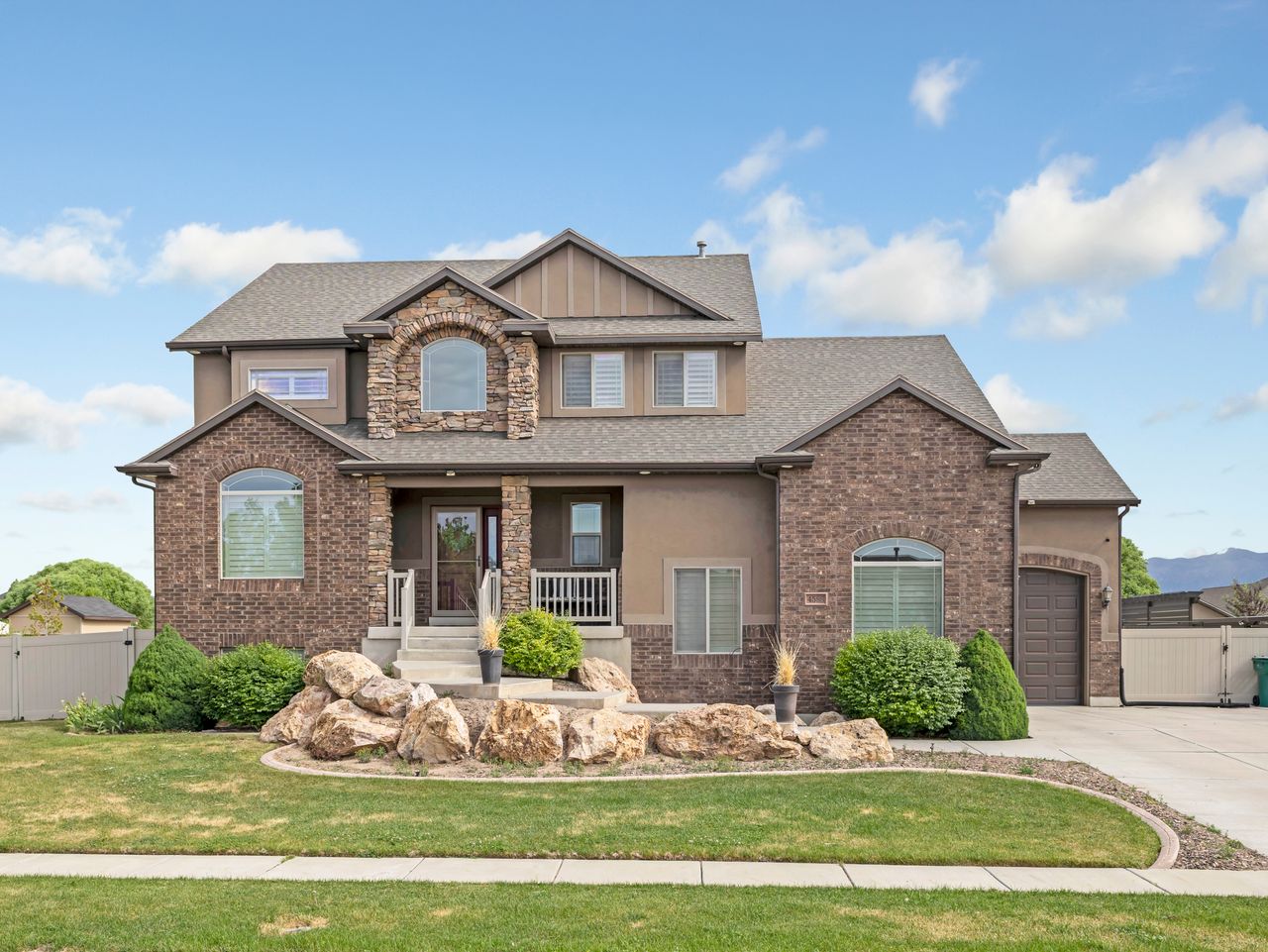 Two-story residence featuring a brick and stone facade, arched windows, covered front porch, an attached garage, and a landscaped front yard with rock accents