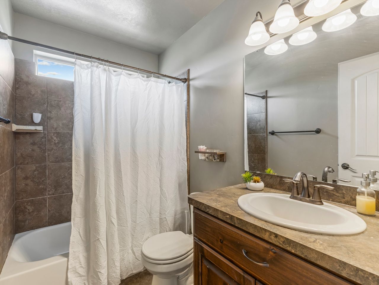 Bathroom featuring a built-in tub with tile surround, a single vanity with a countertop and undermount sink, an overhead light fixture, and a toilet