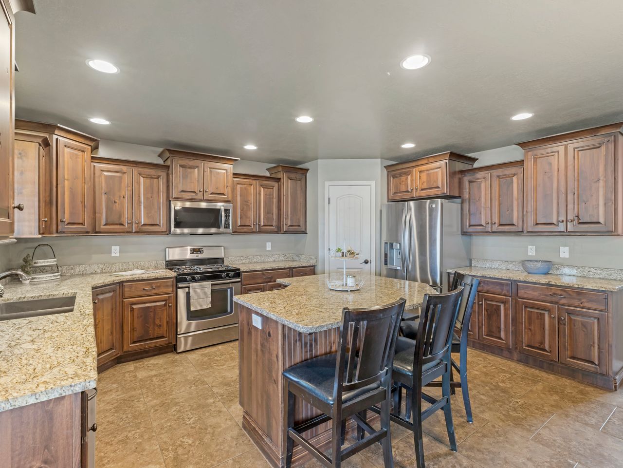 Spacious kitchen featuring extensive wood cabinetry, light-toned granite countertops, and stainless steel appliances