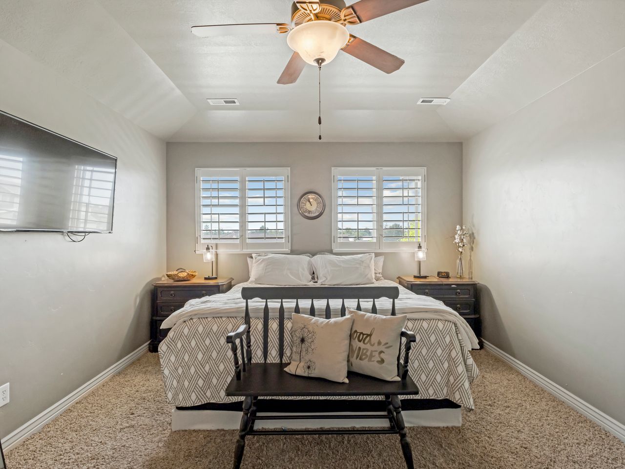 Spacious room featuring vaulted ceilings with a ceiling fan, two windows with plantation shutters, and light-toned carpet flooring