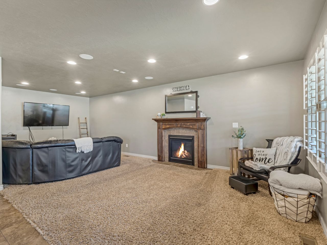 Spacious living area featuring a fireplace with a wood mantle, recessed lighting, carpet flooring, and window shutters