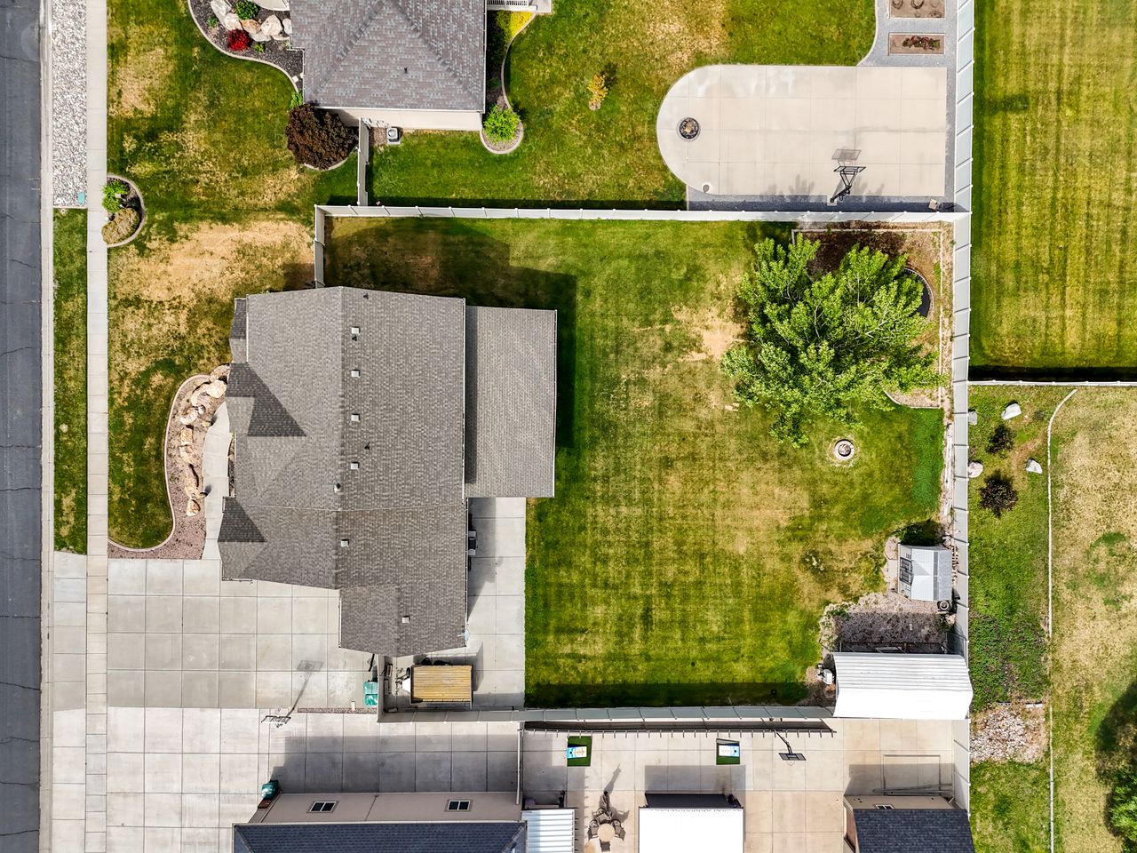 Expansive property featuring a multi-gabled roofline, concrete driveway, mature landscaping with rockery, a substantial green lawn, and an exterior storage shed