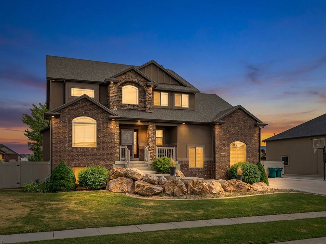 Two-story residential exterior featuring a stone and stucco facade, an arched window, and a stone rockery with integrated landscape lighting