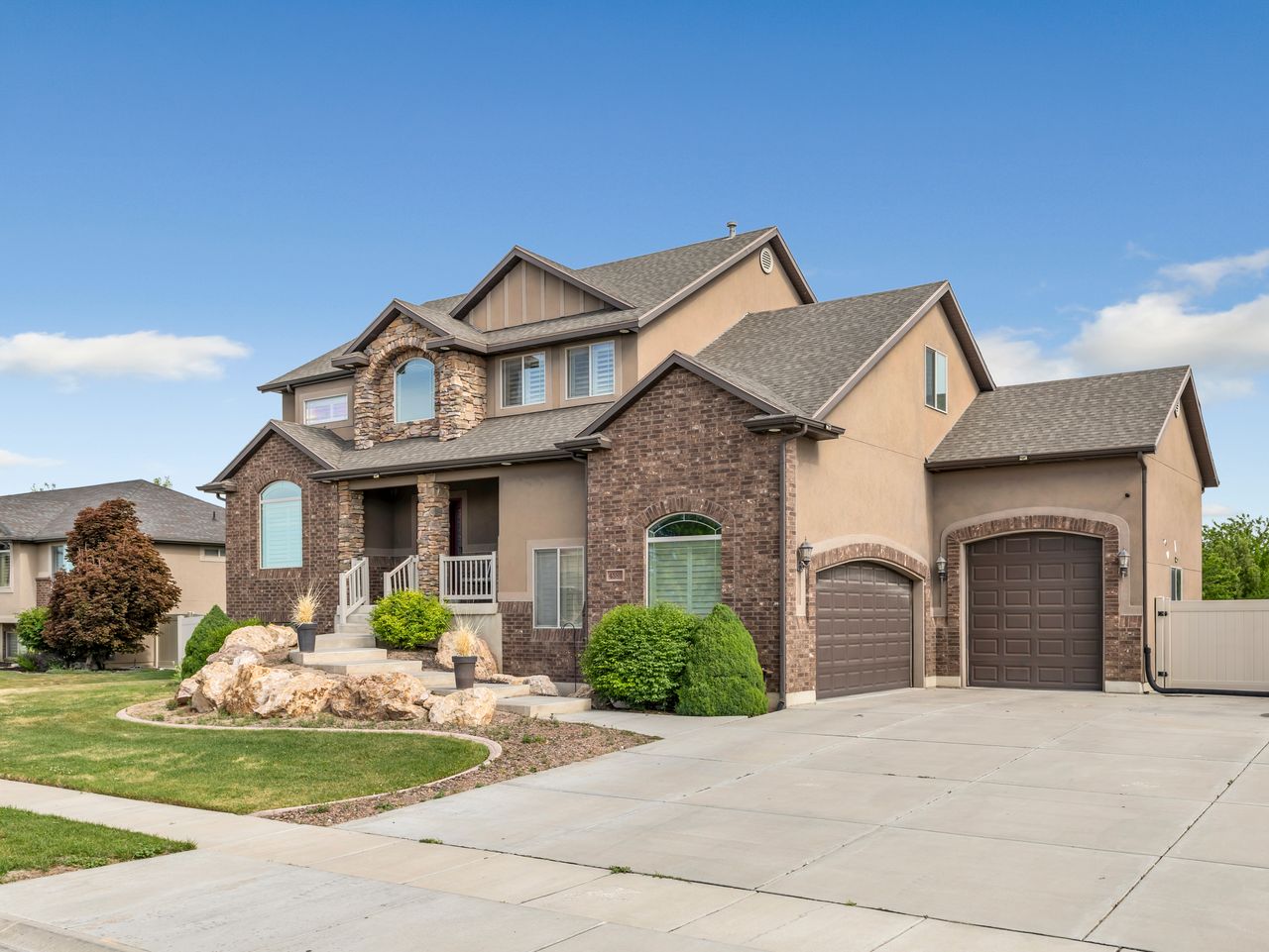 Stately residence featuring a multi-gabled roofline, stone and stucco exterior, arched windows, an inviting front porch with columns, and a two-car garage with arched entrances