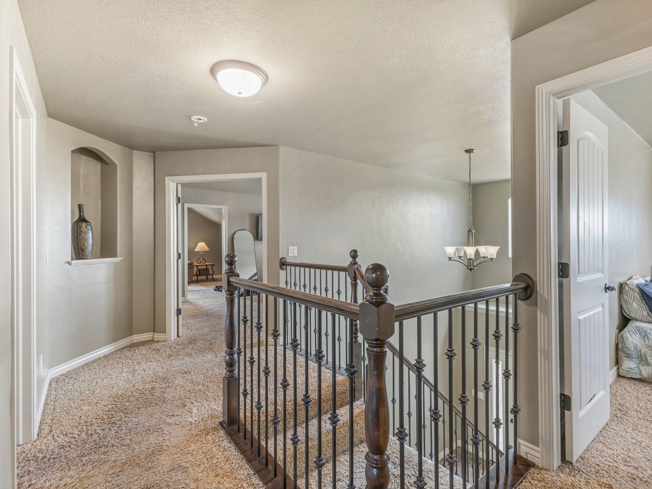 Upper-level hallway featuring a decorative built-in niche, carpet flooring, a dark wood newel post with wrought iron spindles, and a flush-mount ceiling light fixture