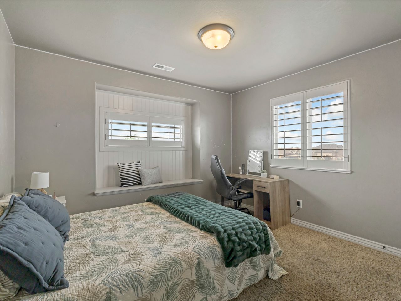 Bedroom featuring neutral wall colors, textured carpeting, and a window with white plantation shutters