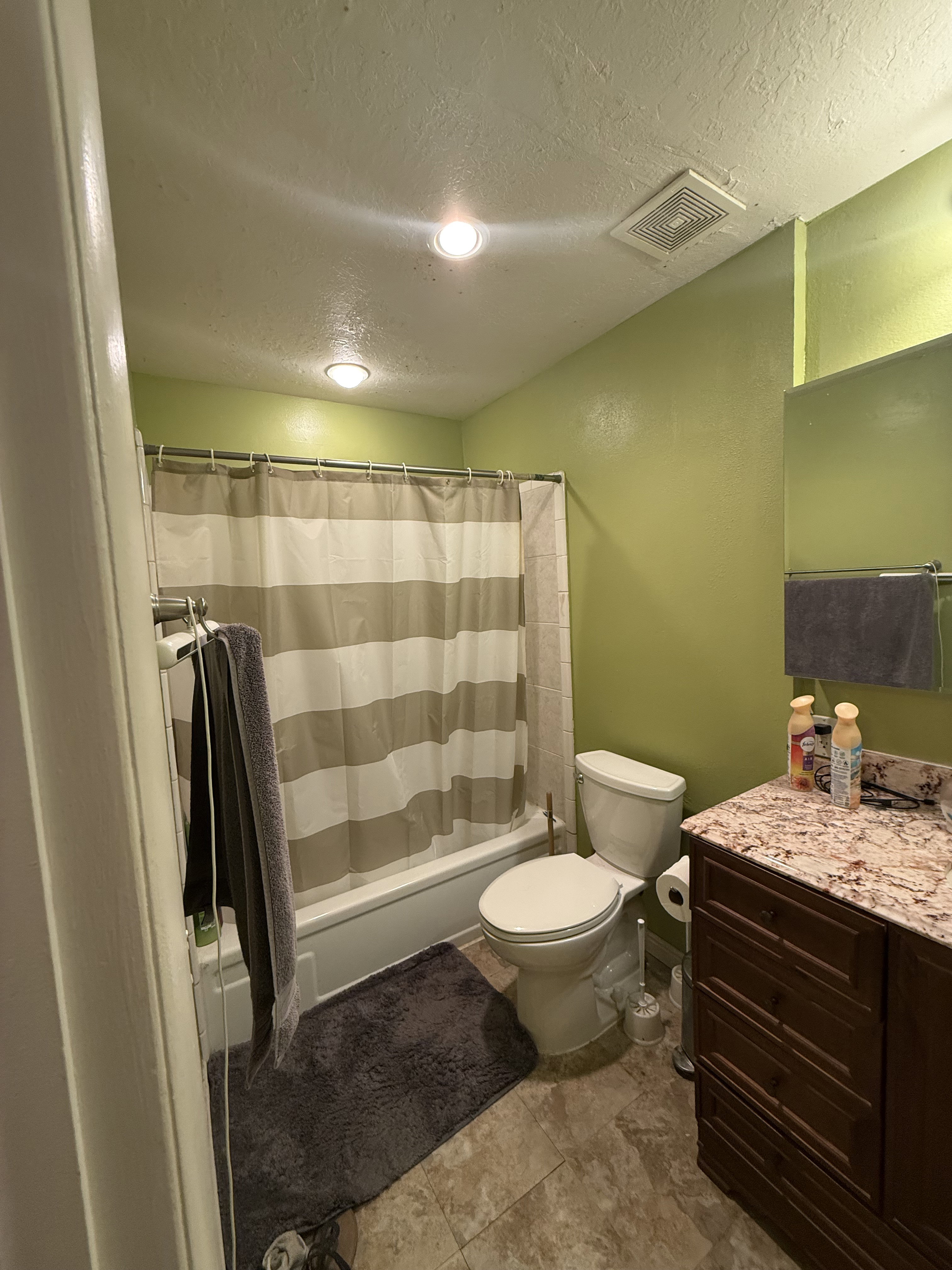 Bathroom featuring a white bathtub with an overhead shower, a white toilet, and a vanity with a stone-look countertop and wood-finish cabinetry