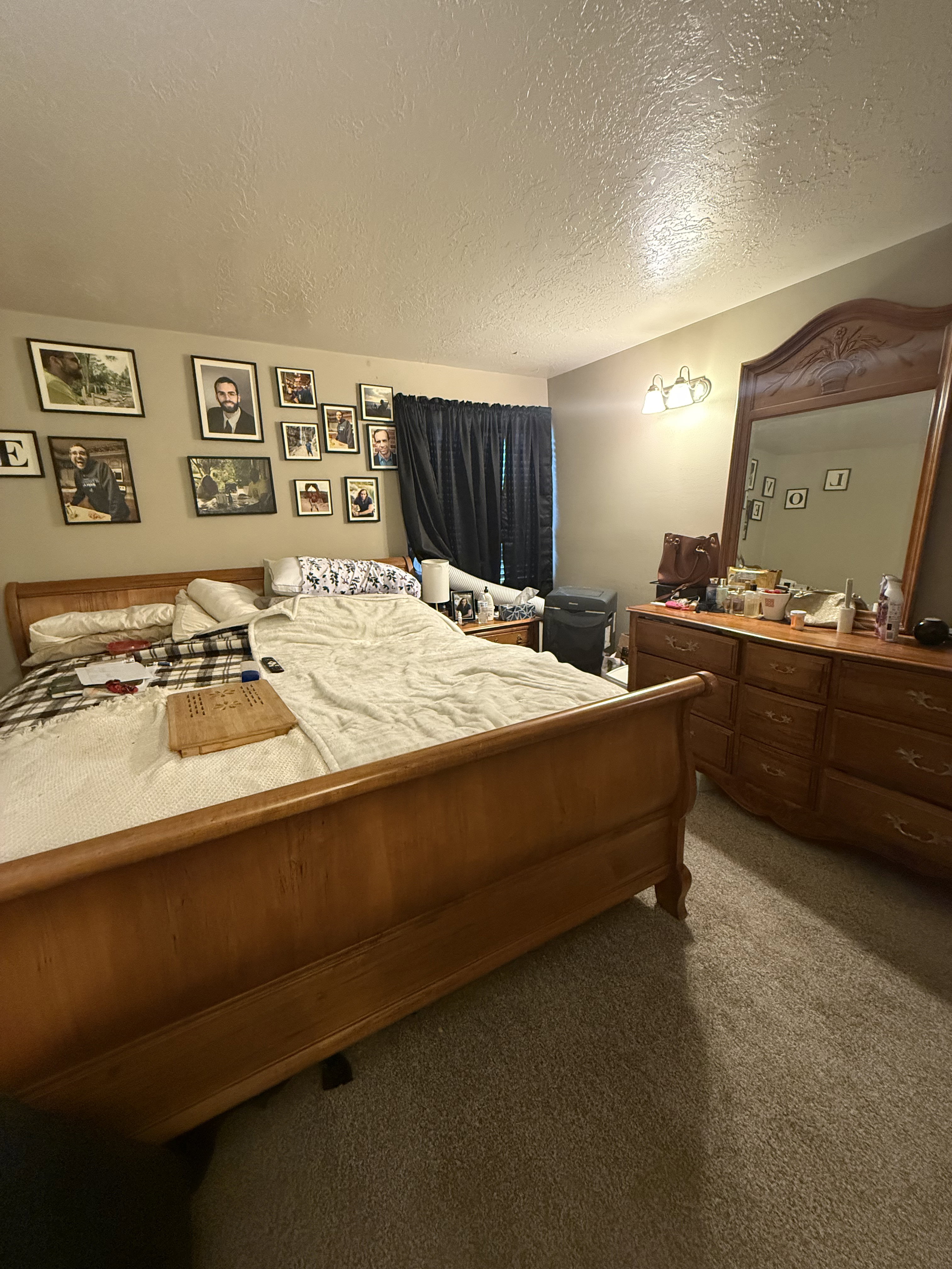 Carpeted room featuring a window with dark drapery, a wall-mounted light fixture, and textured ceilings