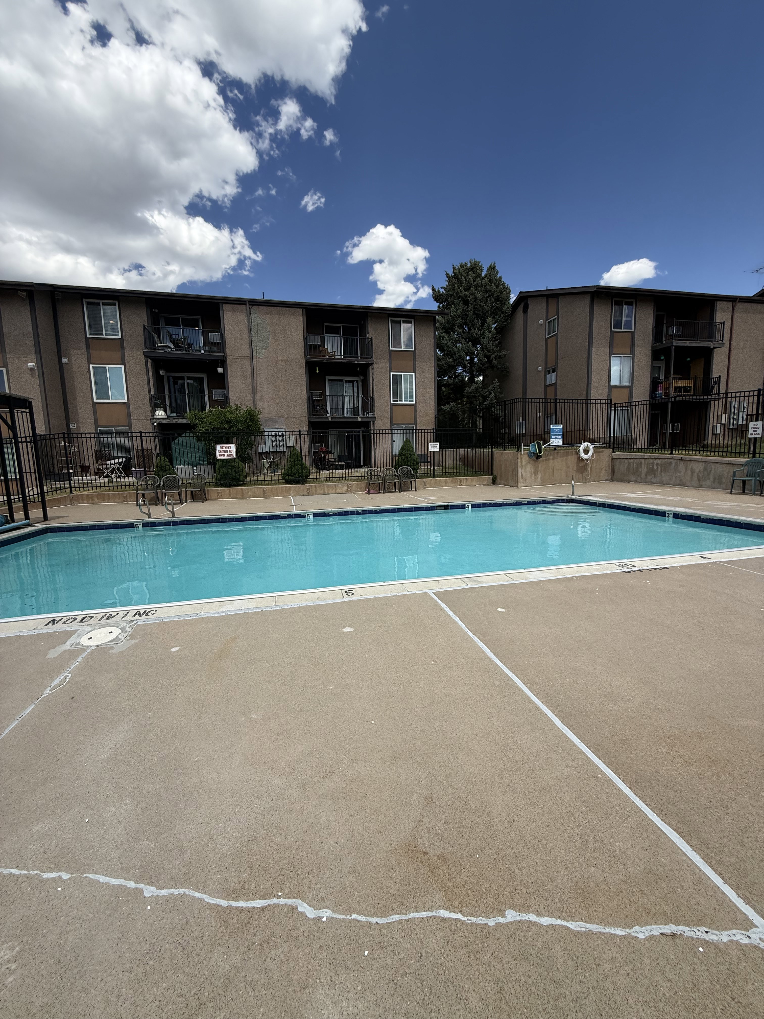 Outdoor swimming pool with concrete decking surrounded by multi-story residential buildings featuring balconies