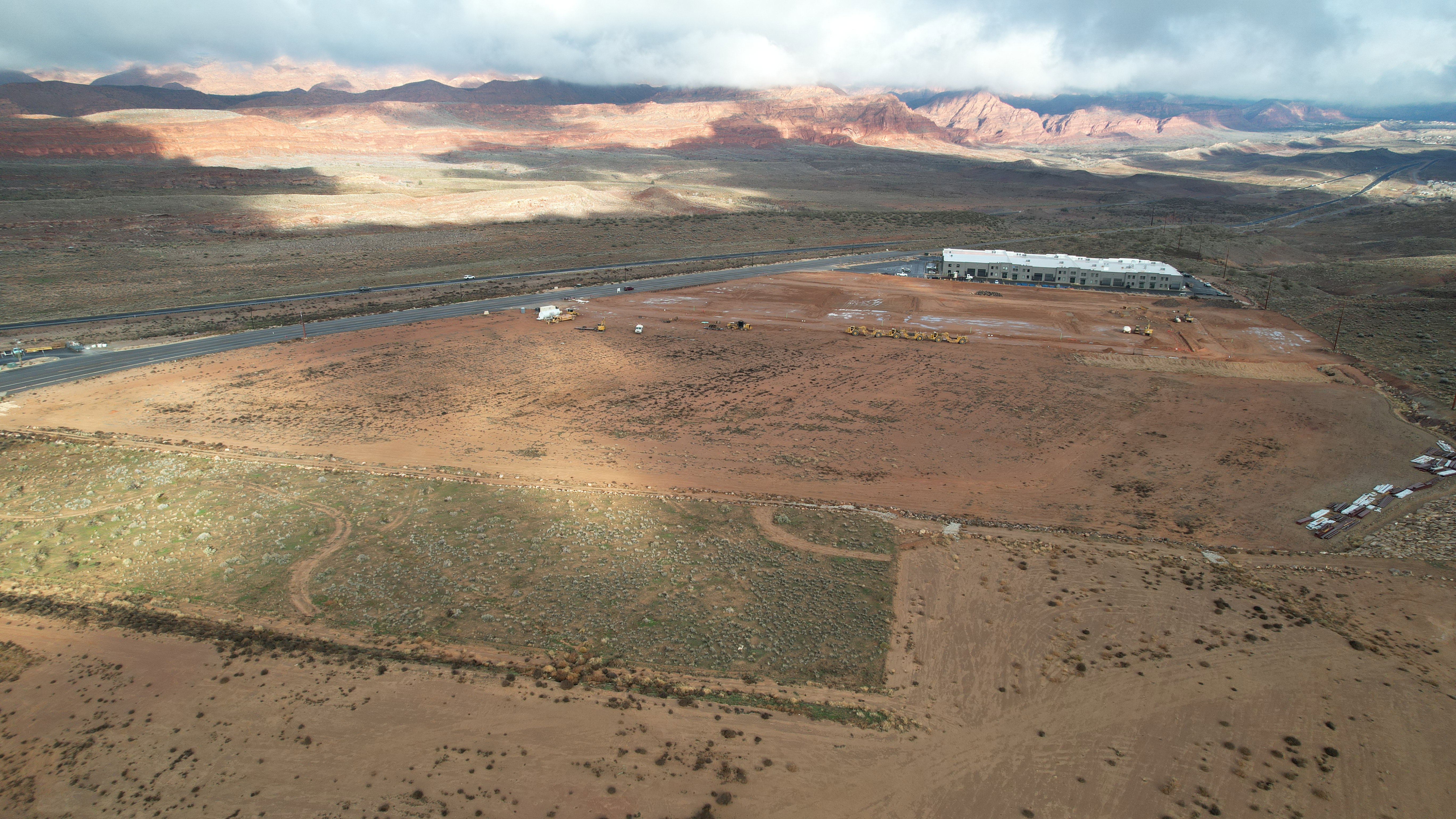 Expansive undeveloped land parcel featuring a paved road frontage, partially graded terrain, and distant rock formations
