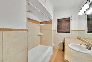 Bathroom featuring a white tub, shower with tile surround, and a vanity with an integrated sink and mirror
