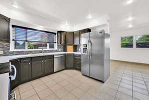 Kitchen featuring dark cabinetry, stainless steel appliances, a tile backsplash, and light countertops