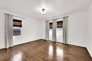 Hardwood flooring throughout, featuring a neutral color palette and three windows with woven blinds