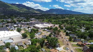 Expansive aerial perspective showcasing a developed area with varied architecture, lush green tree canopy, and mountainous backdrop