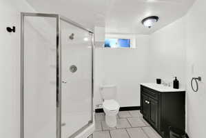 Bathroom featuring an enclosed shower with glass panels, a single vanity with a black cabinet and white countertop, a toilet, and light-toned tile flooring