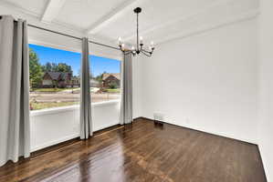 Expansive window wall with white trim, dark wood-finish flooring, a contemporary black chandelier, white textured ceiling, and exposed ceiling beams
