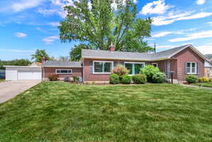Brick exterior with dark shutters, front landscaping, extended driveway, and attached two-car garage