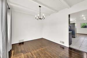 Room featuring exposed ceiling beams, a black iron chandelier, and dark wood-finish flooring