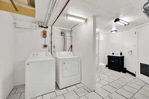 Utility room featuring a washer and dryer, tile flooring, and a separate partially enclosed bathroom area with a dark vanity