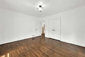 Spacious room featuring rich wood-finish flooring, white baseboards, and a semi-flush mount ceiling light