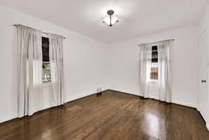 Spacious room featuring rich wood-finish flooring, bright white walls, and two windows allowing natural light