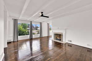 Spacious room featuring rich wood-finish flooring, a prominent white fireplace, and a wide window offering exterior views