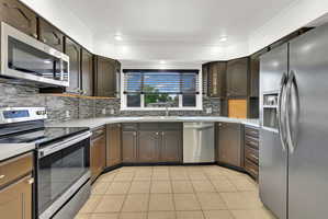 U-shaped kitchen featuring dark wood cabinetry, light-toned countertops, and a mosaic tile backsplash