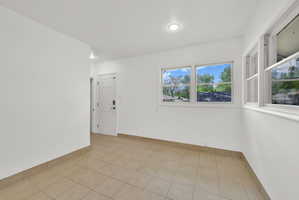 Room featuring neutral tile flooring, white painted walls, multiple windows, a white paneled door, and recessed lighting