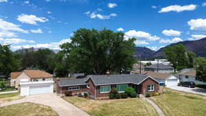 Brick exterior with a dark shingle roof, established landscaping, and a paved driveway leading to an attached garage