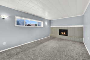 Spacious room featuring a brick fireplace with a raised hearth, light blue walls, and grey carpeting